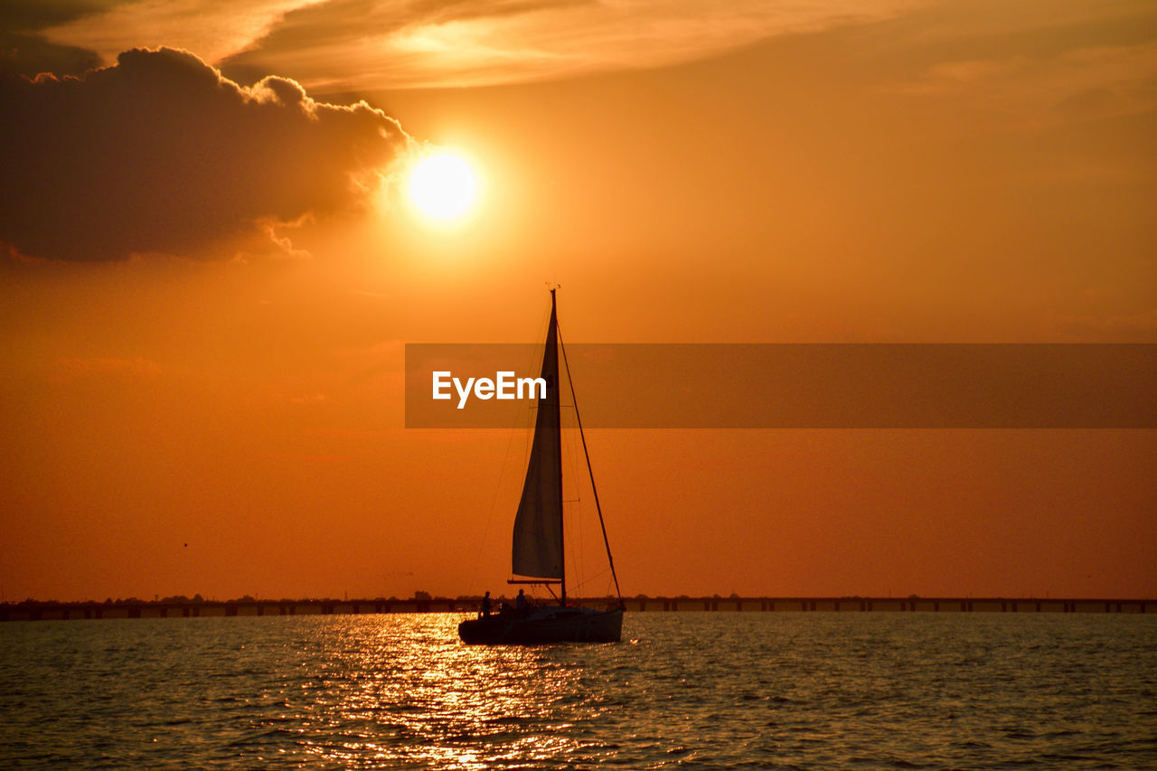 Silhouette sailboat sailing on sea against sky during sunset