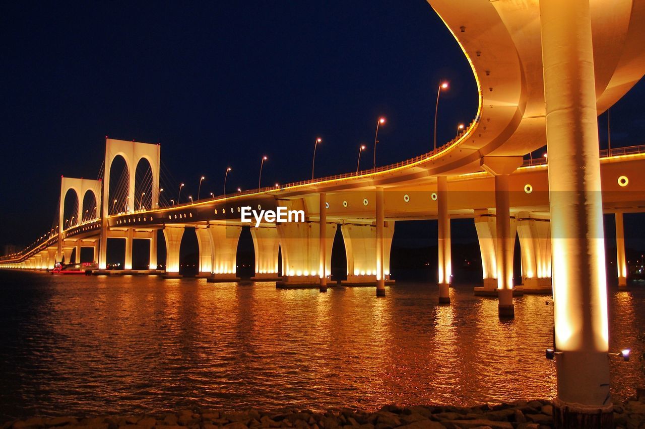 Illuminated bridge over river against sky at night