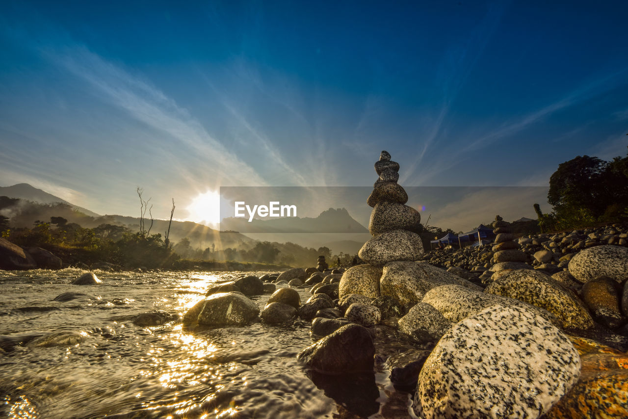 Low angle view of stones stacked by river against sky