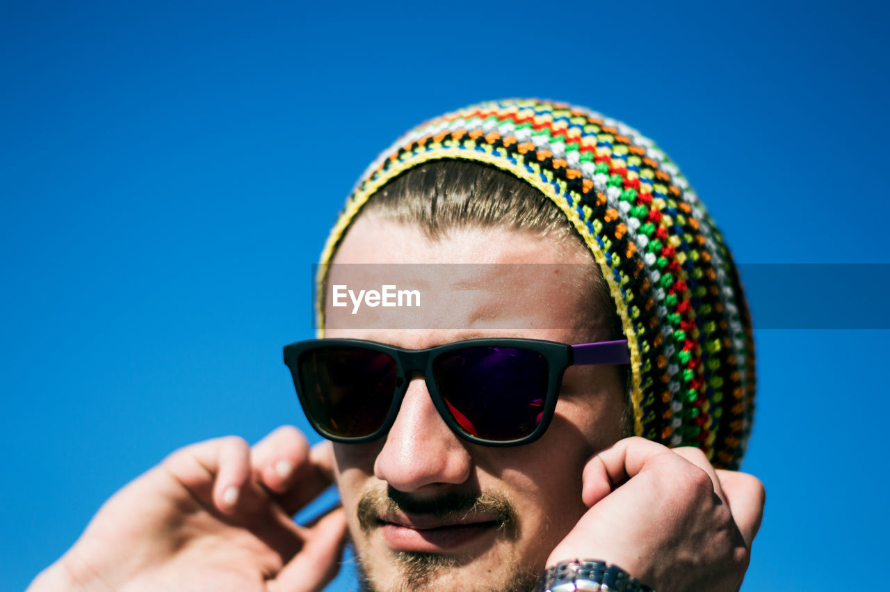 Close-up of young man wearing sunglasses against clear blue sky