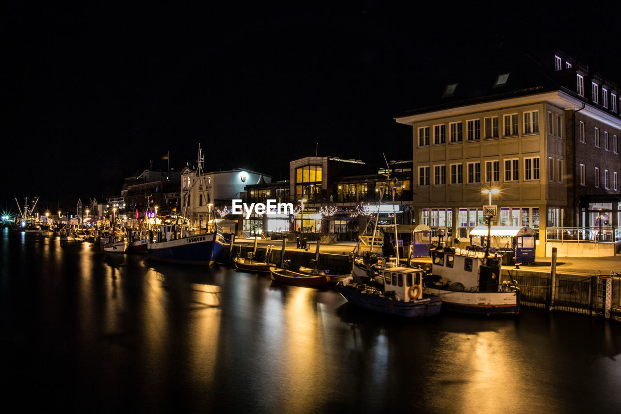 Boats moored at harbor against houses at night