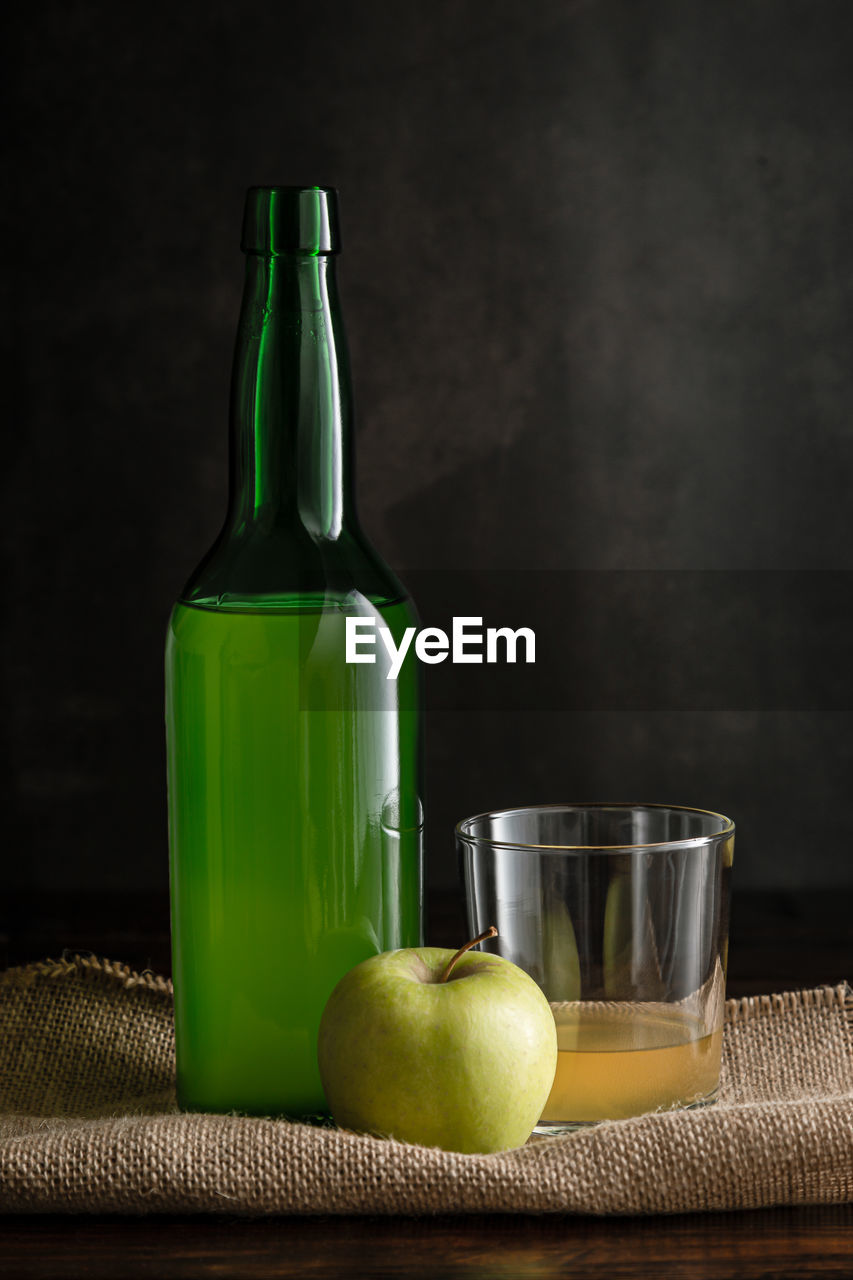 Bottle of asturian cider with glass and apple on dark background with copyspace. vertical format.