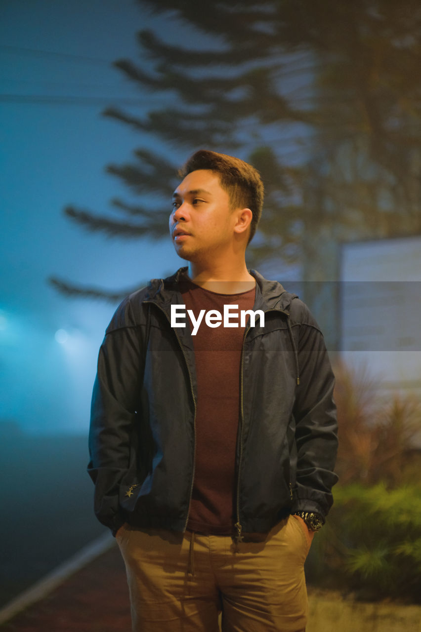 Young man looking away while standing outdoors at night