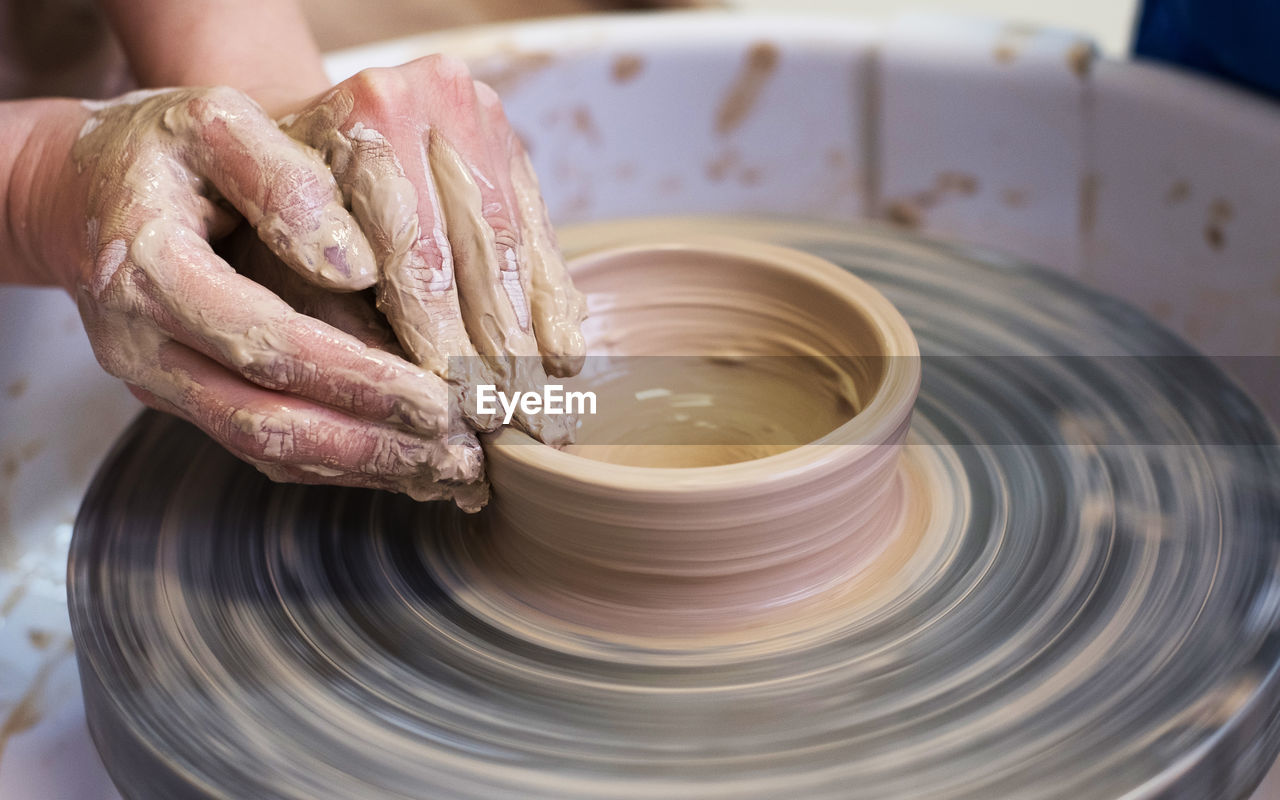 Women's hands make a plate of clay on a potter's wheel.