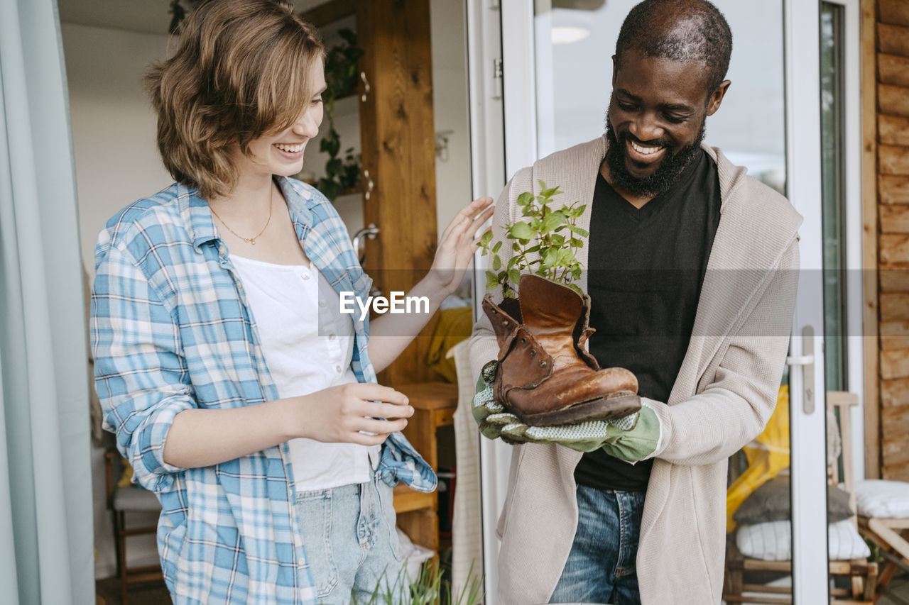 Happy mature man showing plant in leather boot to woman while standing on porch