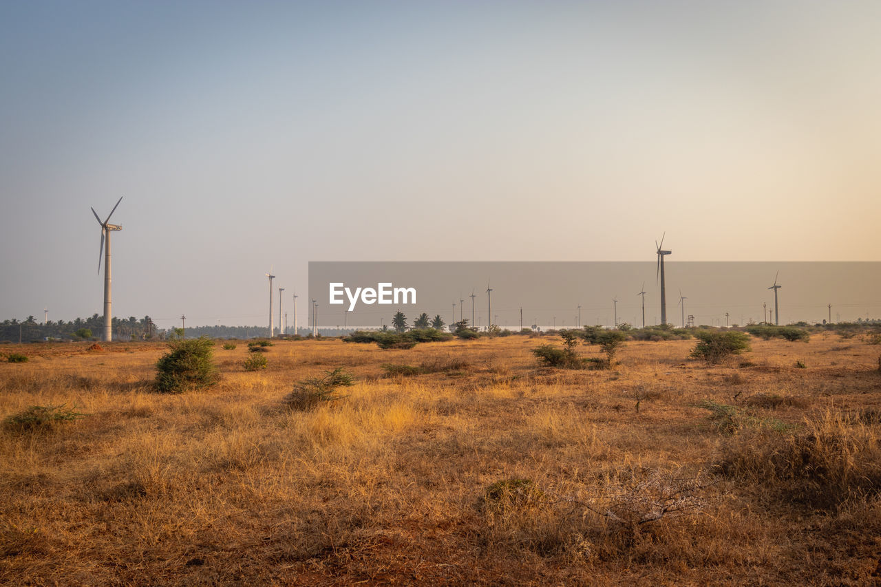 Wind turbines on field against sky during sunset