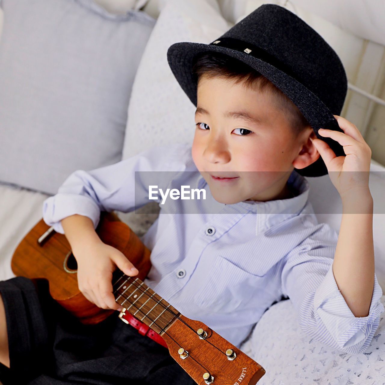 Portrait of cute boy with guitar sitting on sofa at home