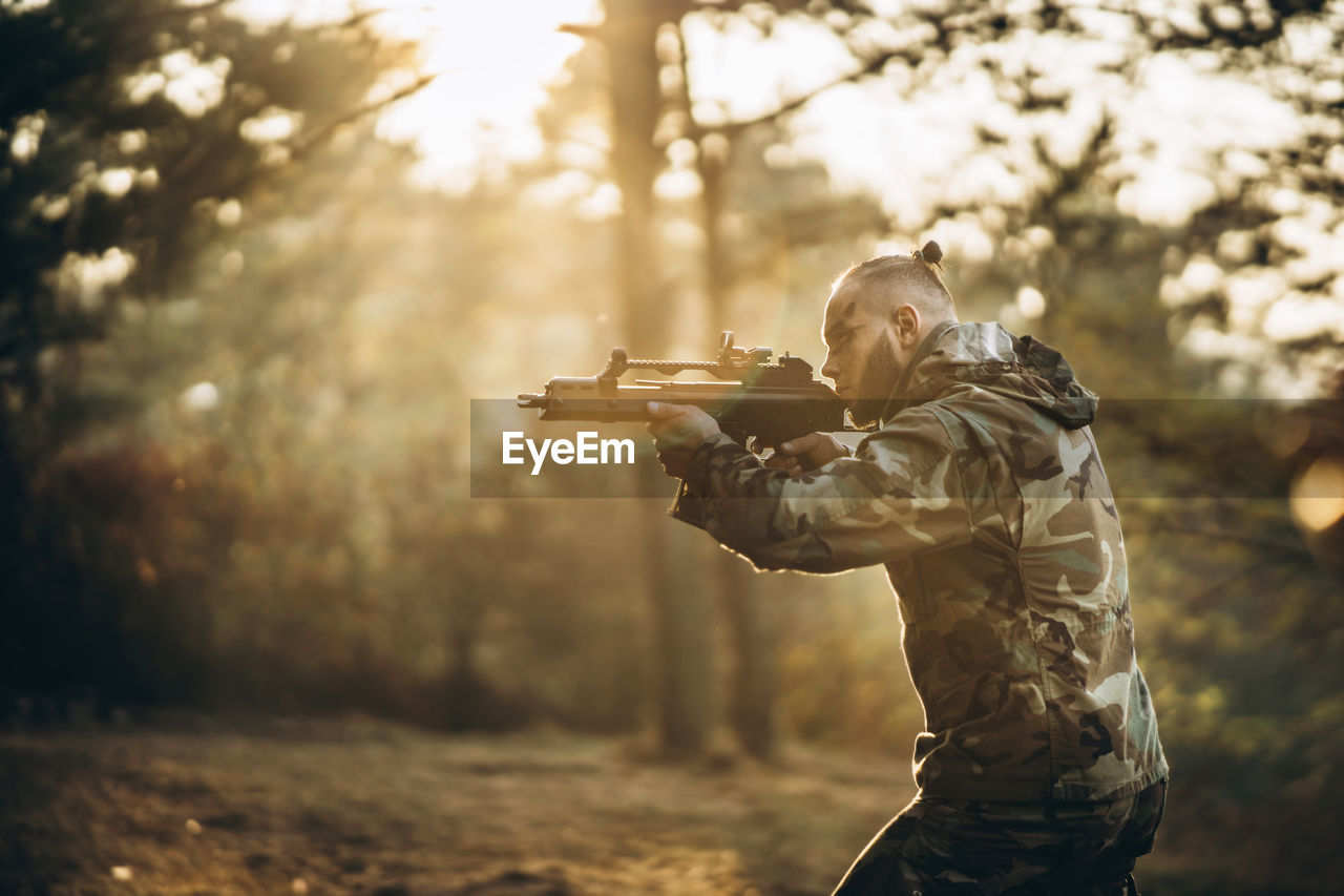 Side view of army soldier aiming gun in forest