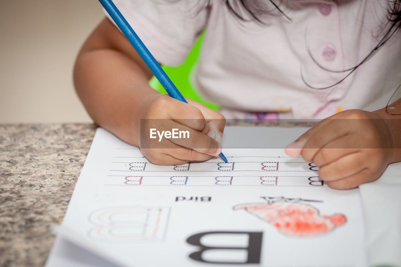 Midsection of girl tracing alphabet at home