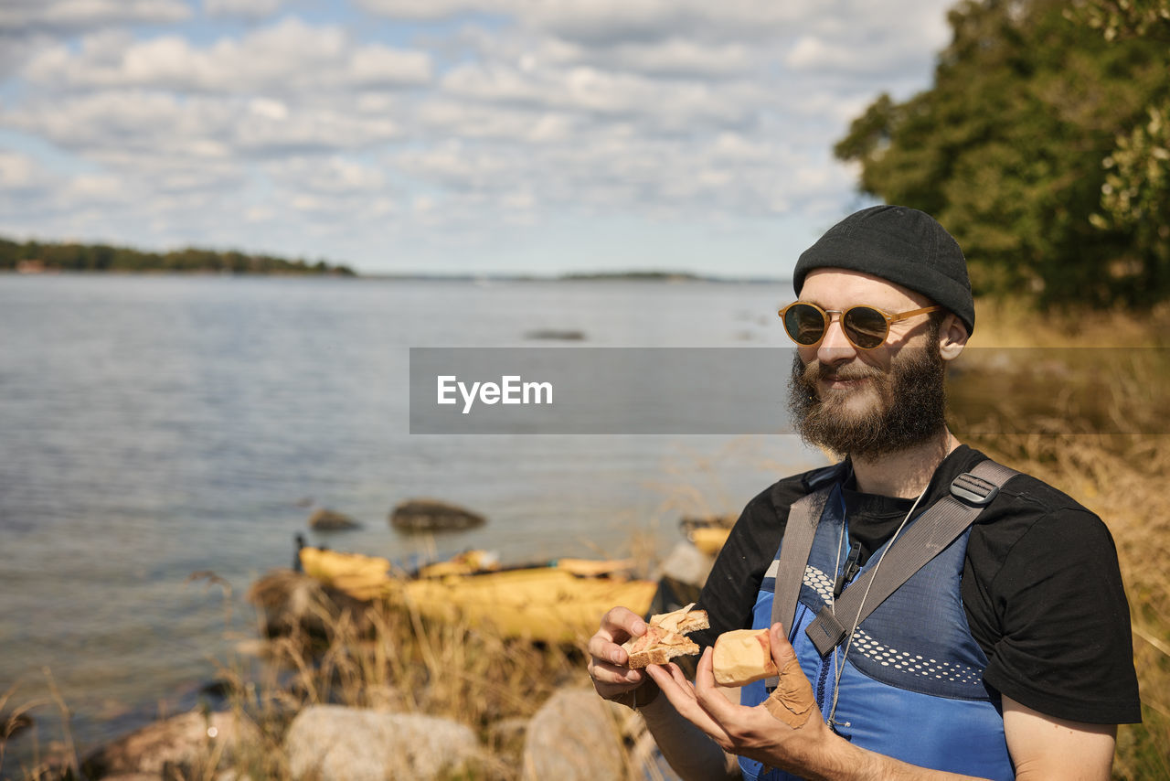 Smiling man at lake wearing jacket and holding food