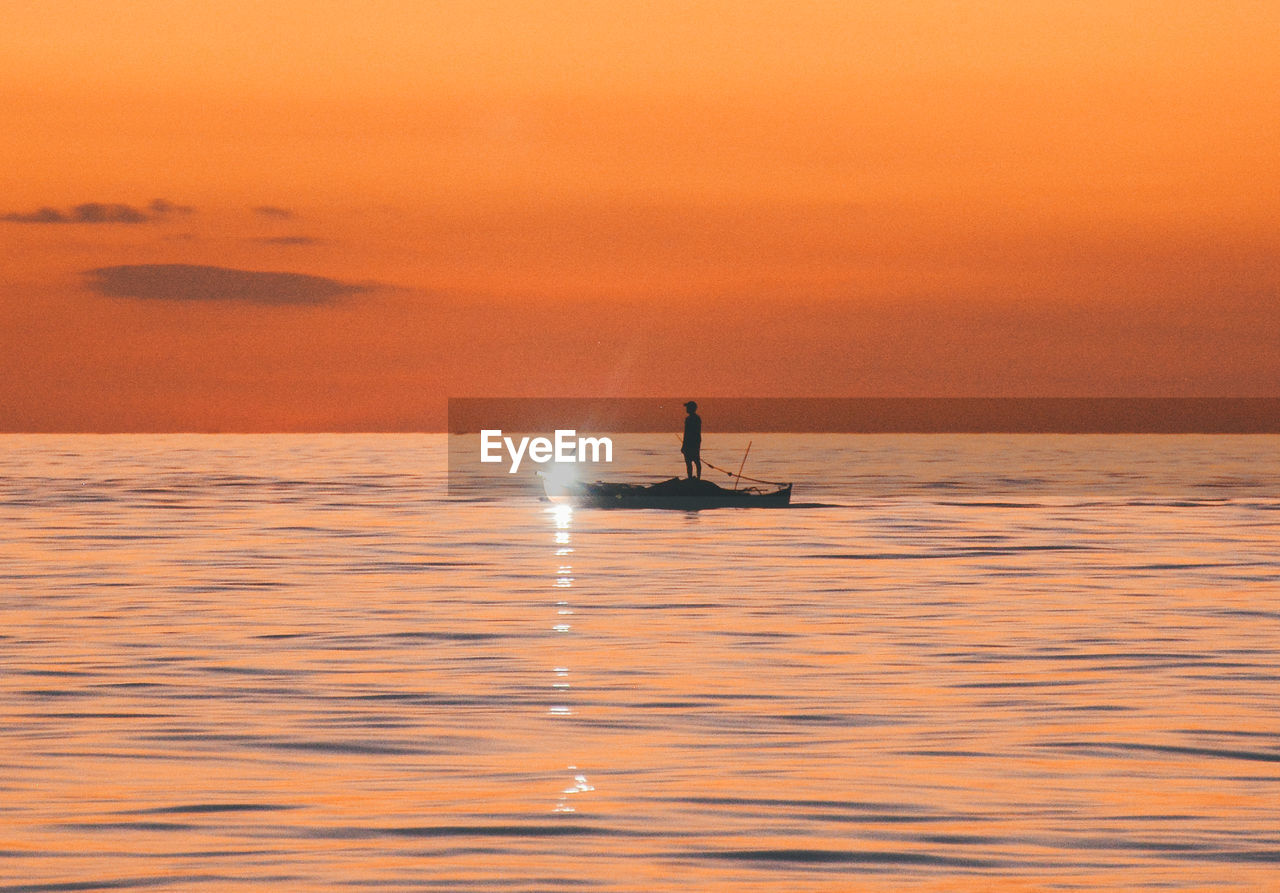 Silhouette man in sea against sky during sunset