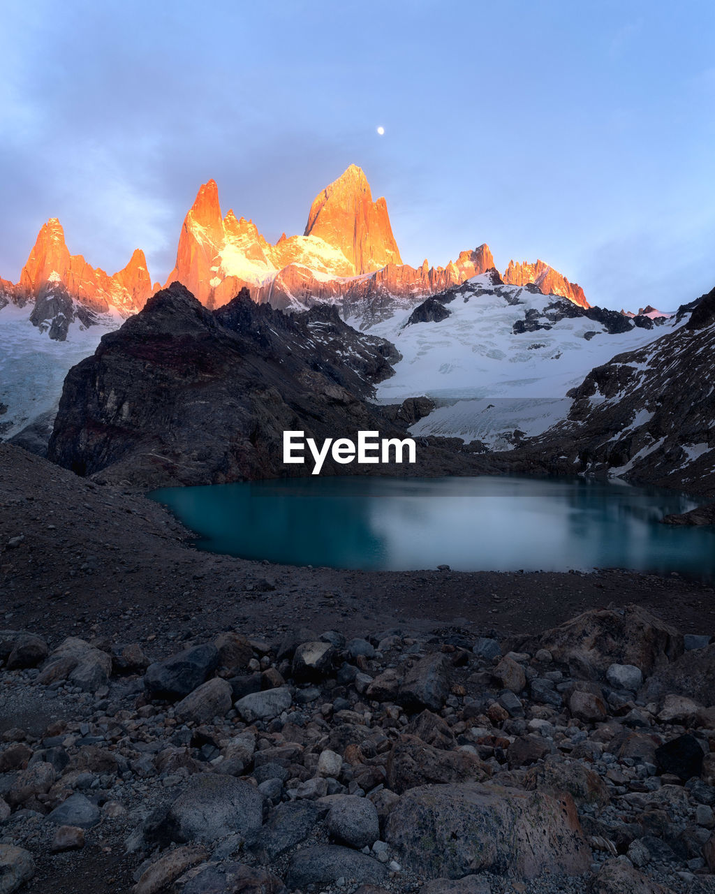 Scenic view of lake by snowcapped mountains against sky during sunset