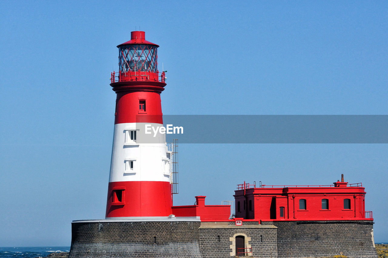 lighthouse by building against sky