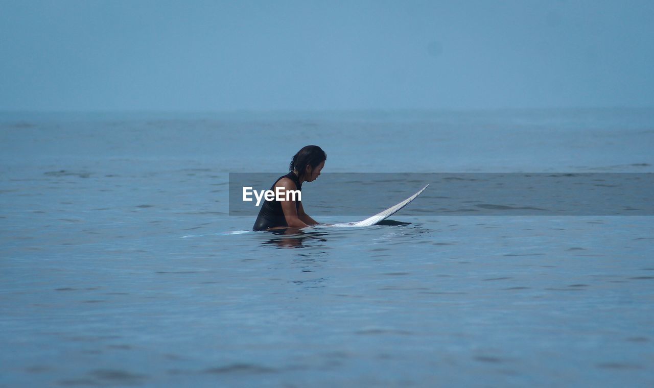 Side view of woman sitting on surfboard in sea
