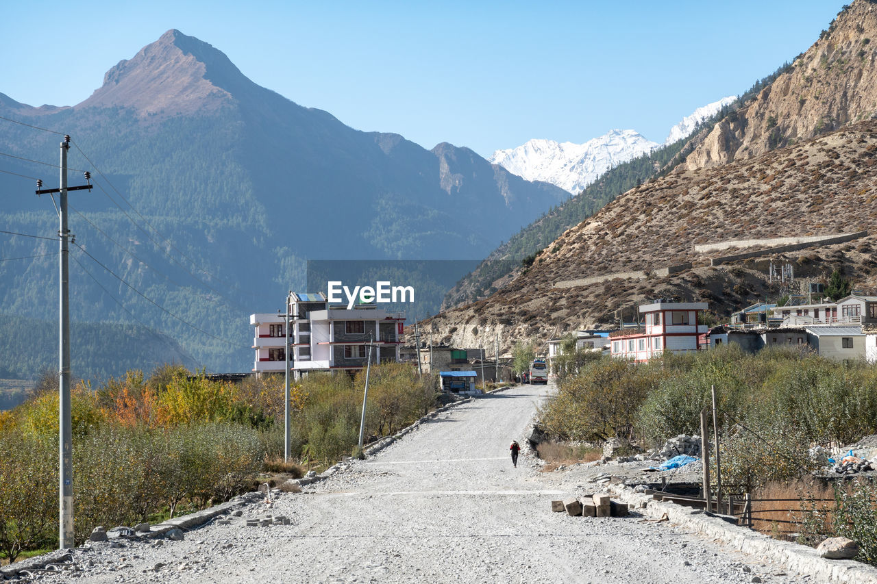 Road by houses and mountains against clear sky