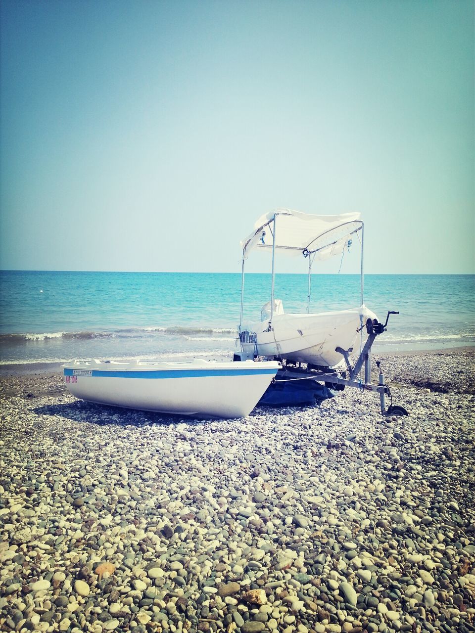 Boats moored on pebble beach against sea and clear sky