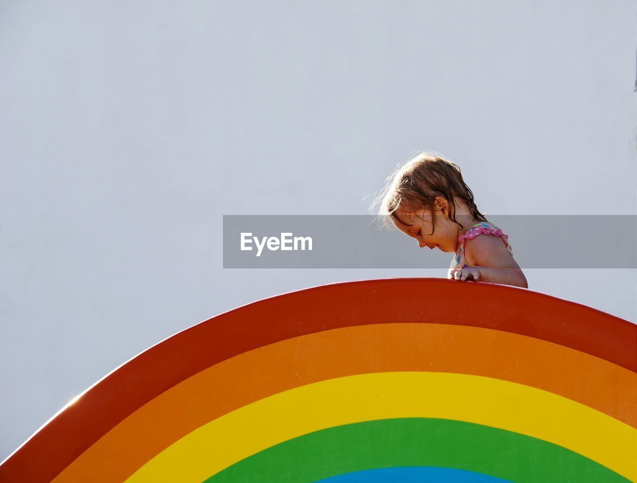 Low angle view of girl on top of rainbow  against sky
