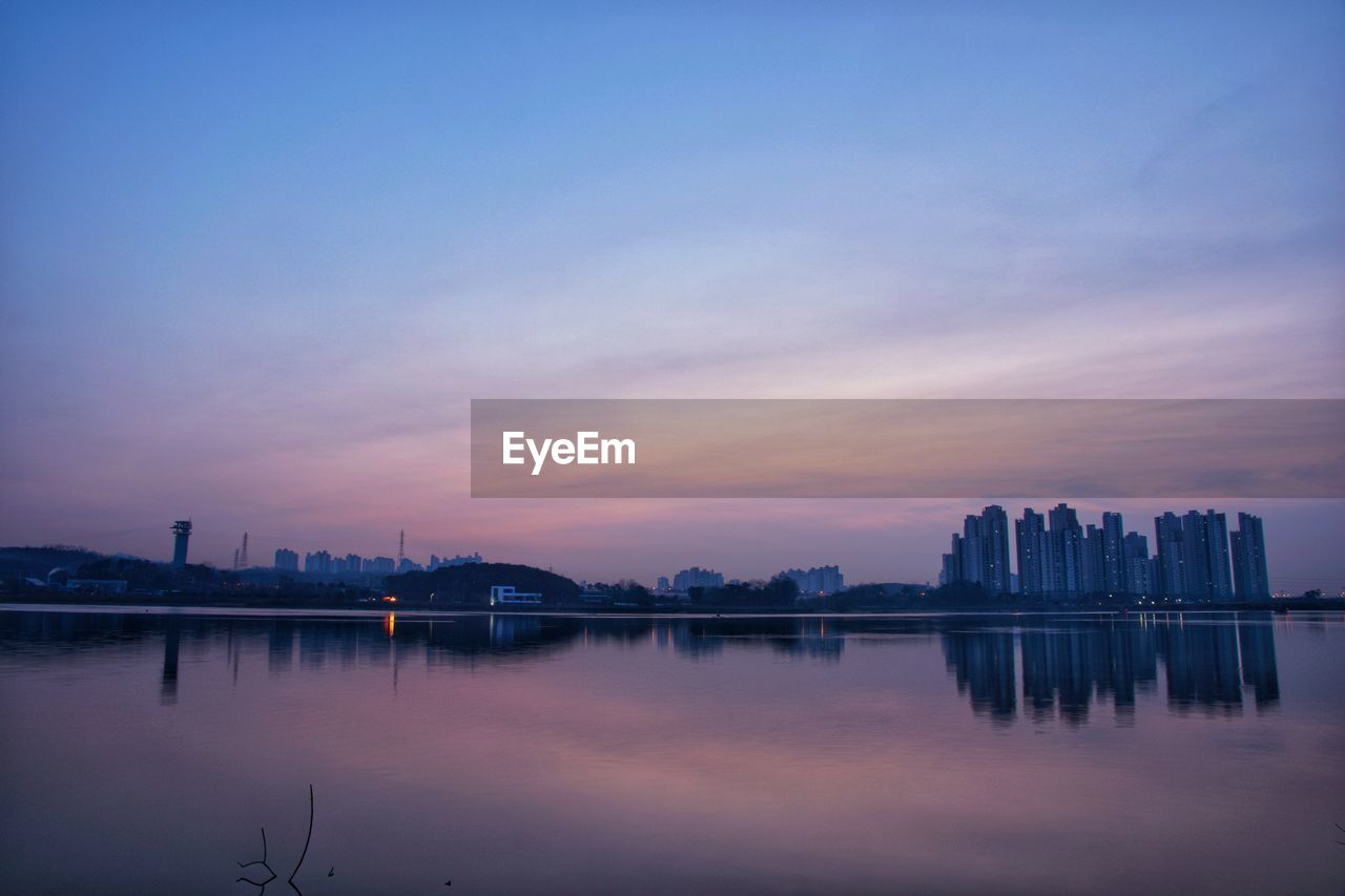 Scenic view of lake by buildings against sky at sunrise