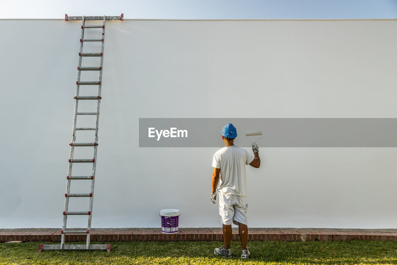 Unrecognizable young painter painting the facade of an apartment with a roller with the ladder on the side