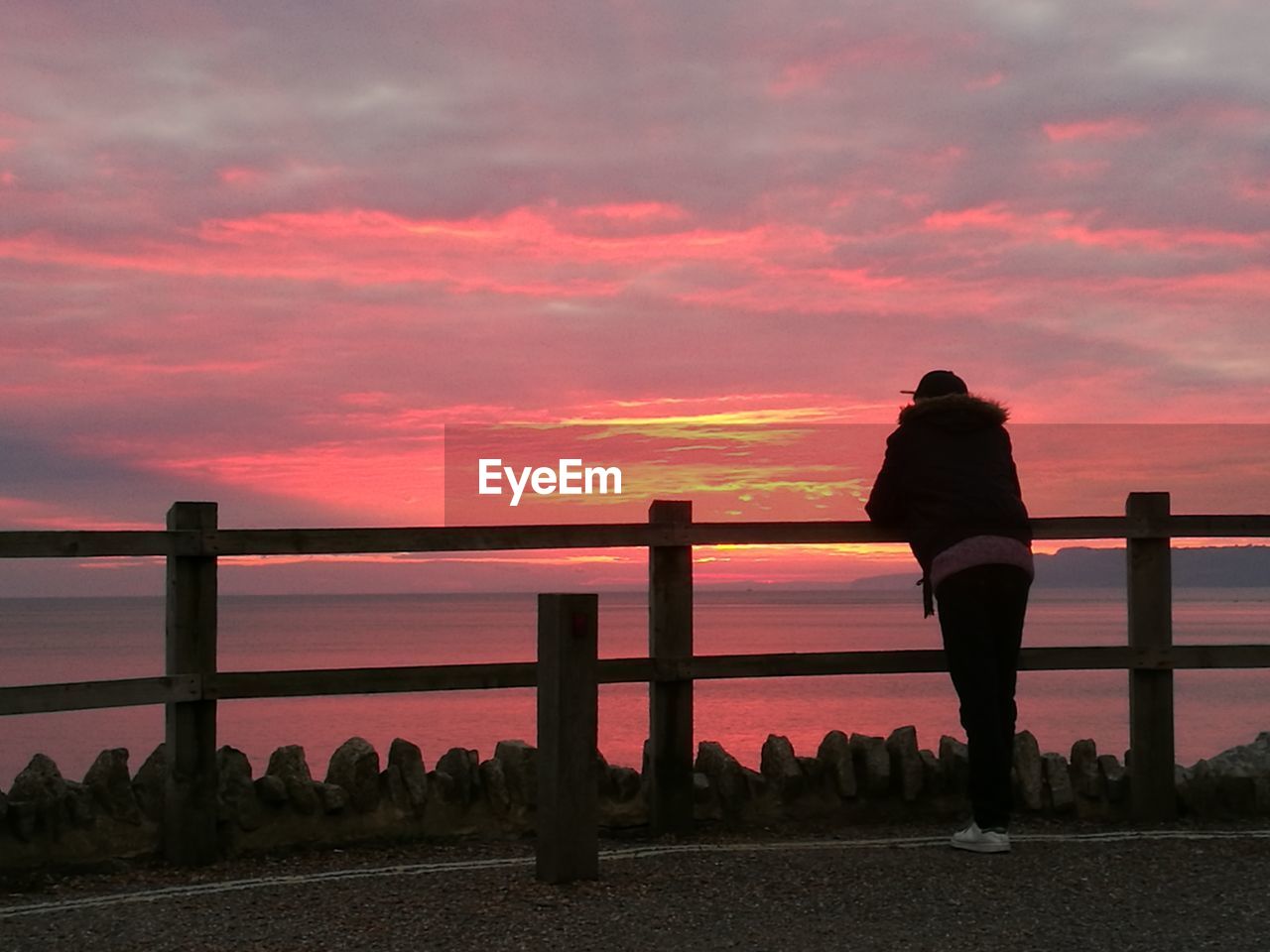 SILHOUETTE MAN STANDING ON RAILING AGAINST SEA