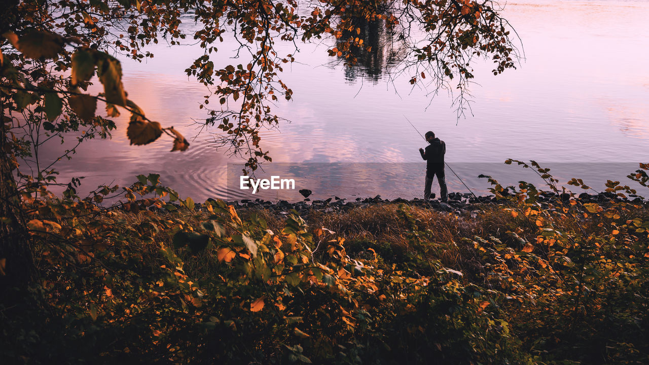 SILHOUETTE OF MAN STANDING BY LAKE AGAINST SKY