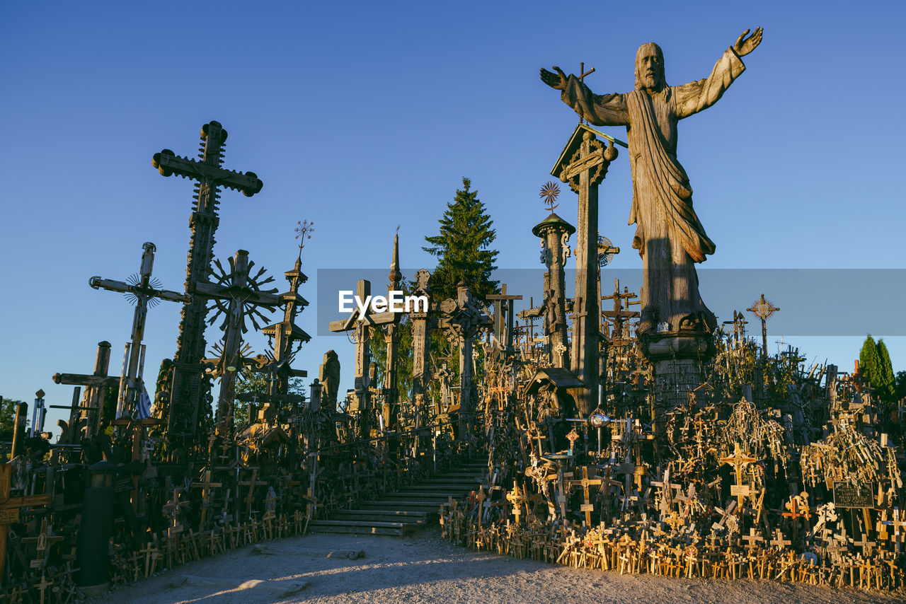 Statue and cross at cemetery against clear sky