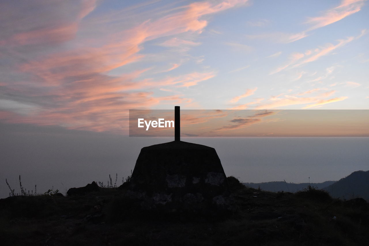 CROSS ON ROCK AGAINST SKY DURING SUNSET