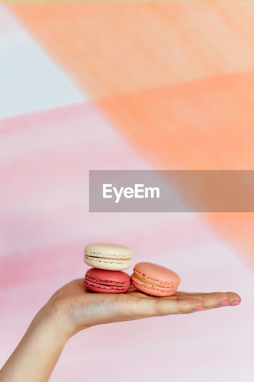 Close-up of hand holding macarons against blurred background
