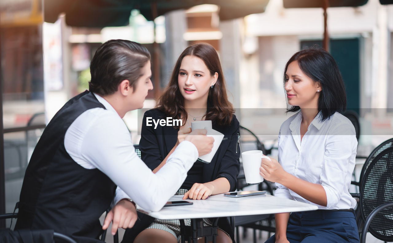 Business people toasting drinks while sitting at sidewalk cafe