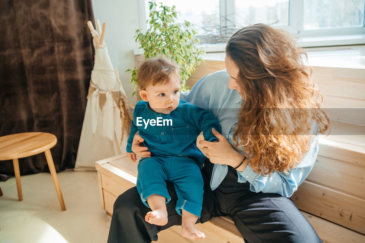 Mother with baby son on the background of a window and a wooden bench. high quality photo