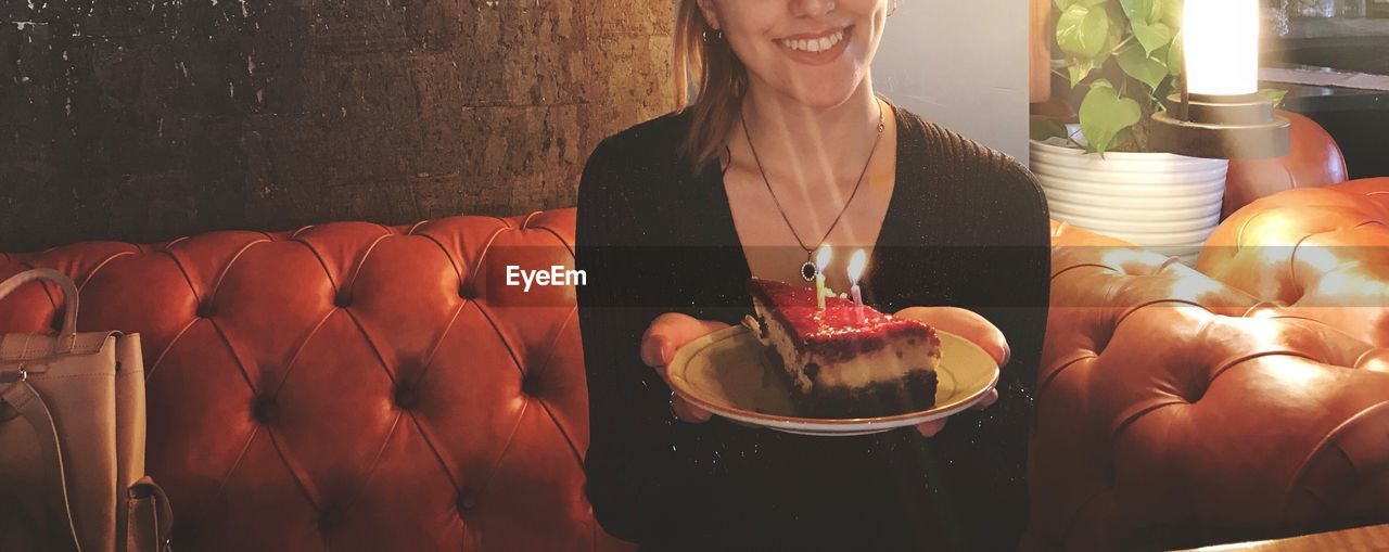 Midsection of woman holding plate with cake while sitting on sofa at home