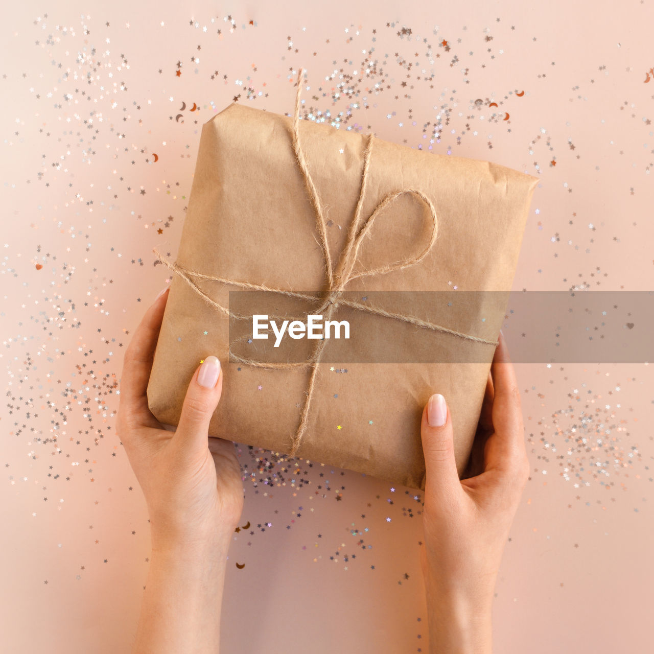 Female hands with natural manicure holding present in kraft paper with jute on beige background