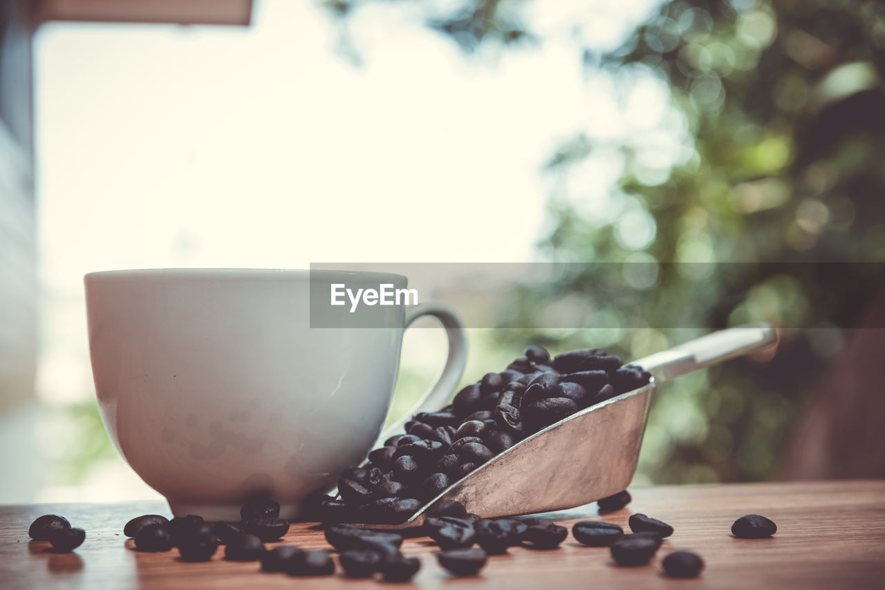 Close-up of roasted coffee beans with cup on table