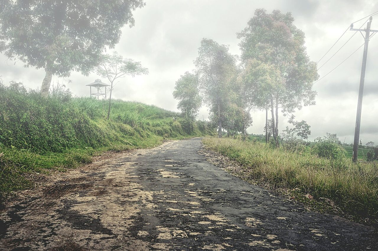 Dirt road amidst field against cloudy sky