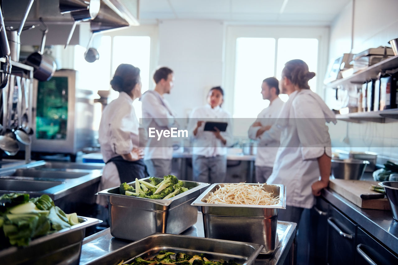 Vegetables in containers with chef team discussing in background at kitchen