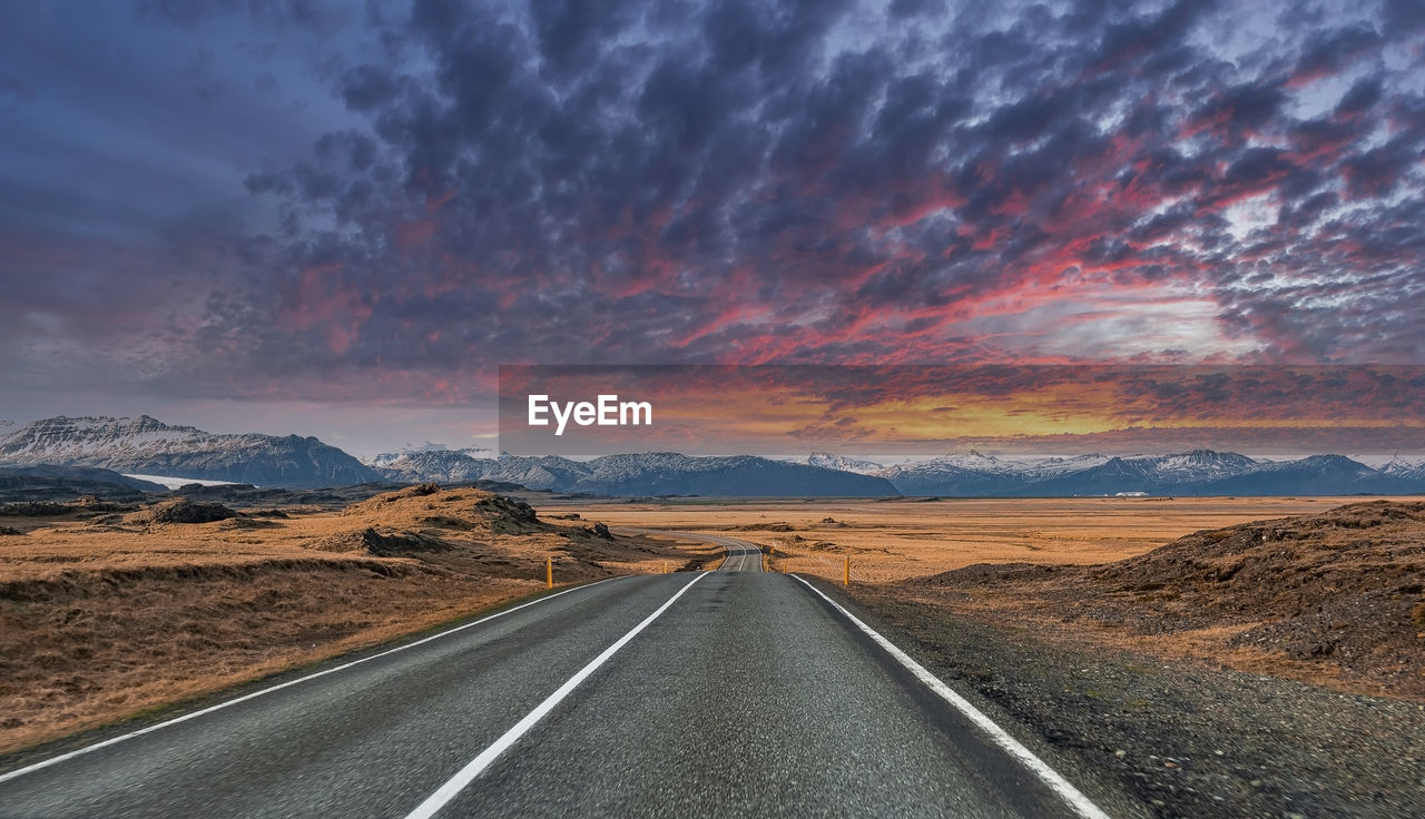 Empty vanishing road amidst volcanic landscape against cloudy sky during sunset