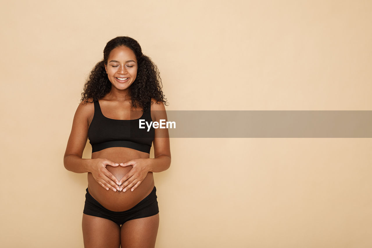 Smiling pregnant woman against beige background