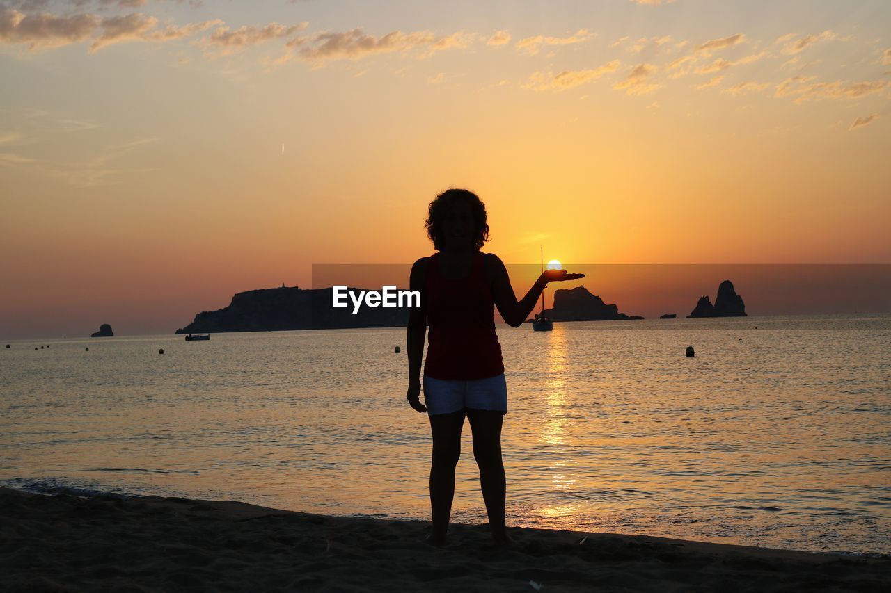 REAR VIEW OF SILHOUETTE STANDING ON BEACH DURING SUNSET