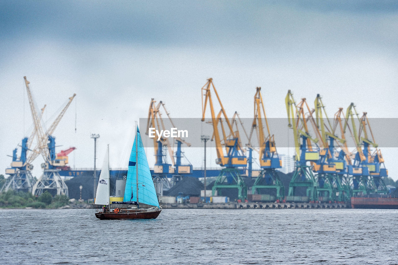 Boat sailing on sea against cranes