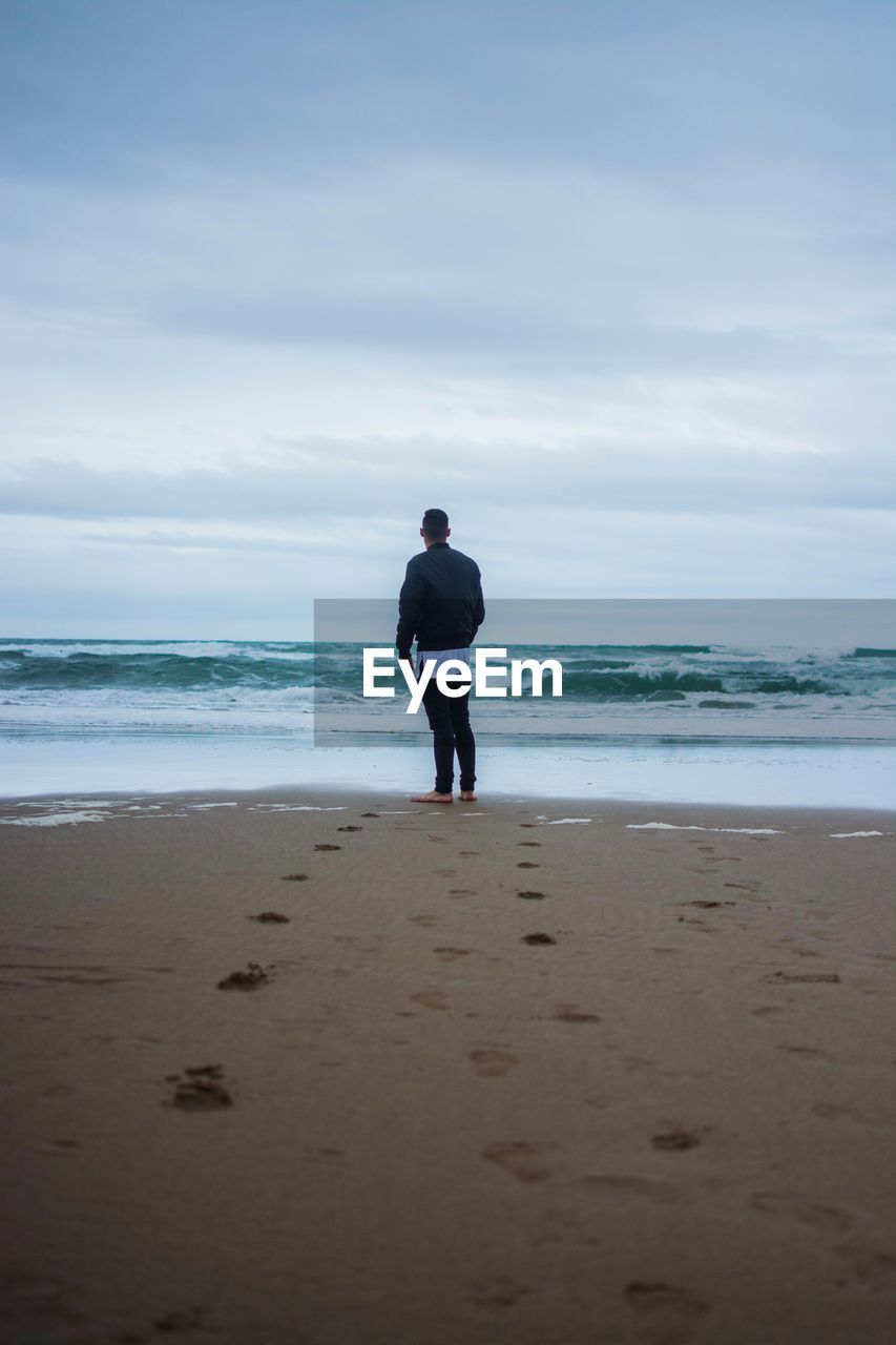 Rear view of man looking at sea while standing on shore against sky