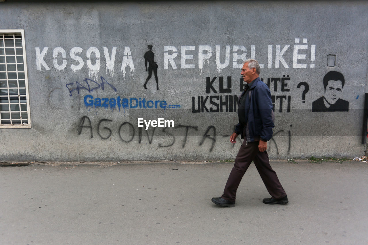 FULL LENGTH OF MAN STANDING BY TEXT ON WALL