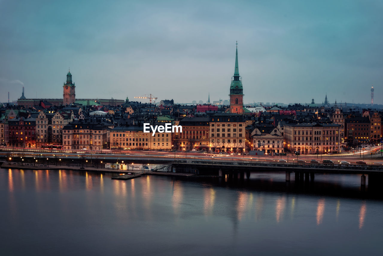 Illuminated buildings by river against sky in city