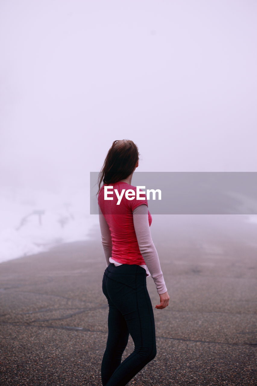 Rear view of young woman standing road during foggy weather