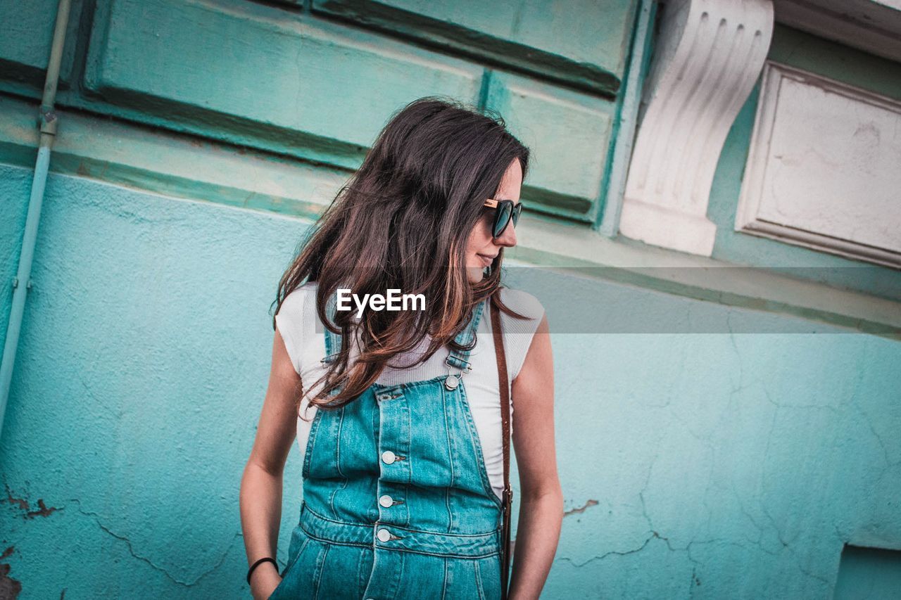 Woman wearing sunglasses while standing against wall