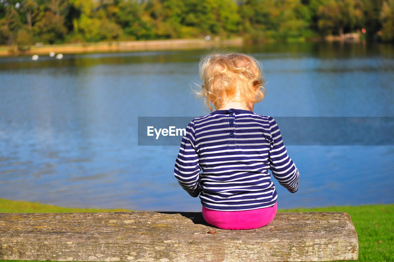 Rear view of girl sitting on bench by lake