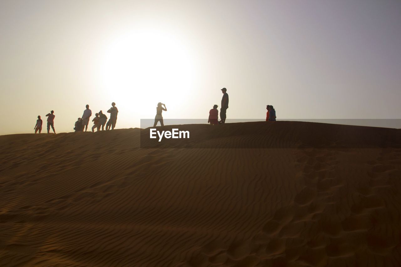 People on sand dune in desert against clear sky