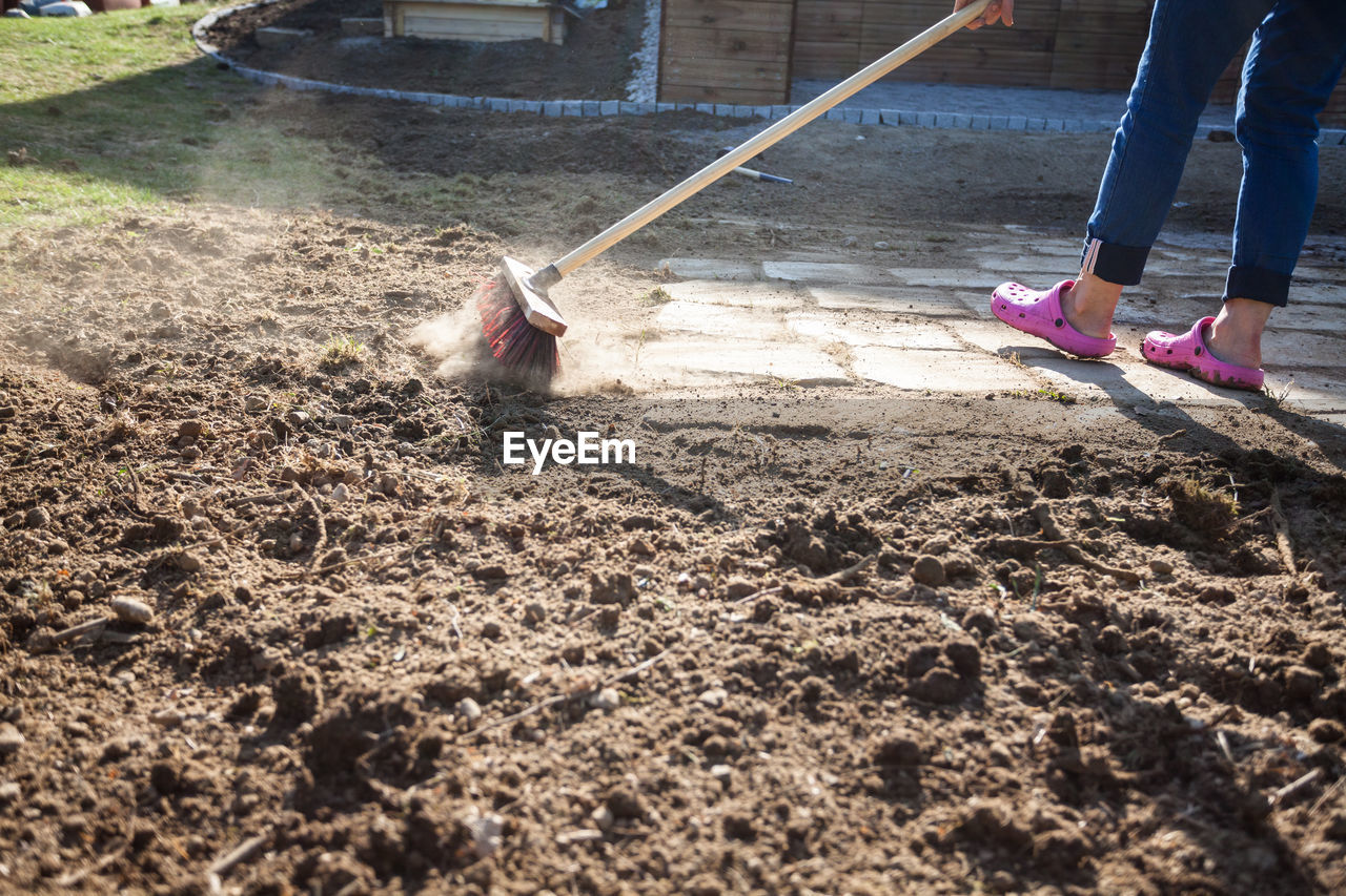 Low section of woman cleaning ground in backyard