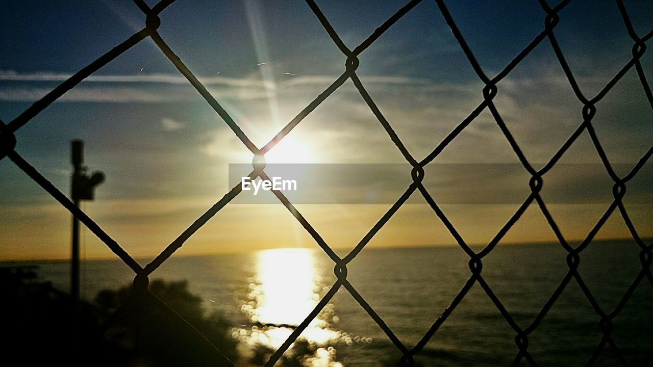 Close-up of chainlink fence against sky during sunset