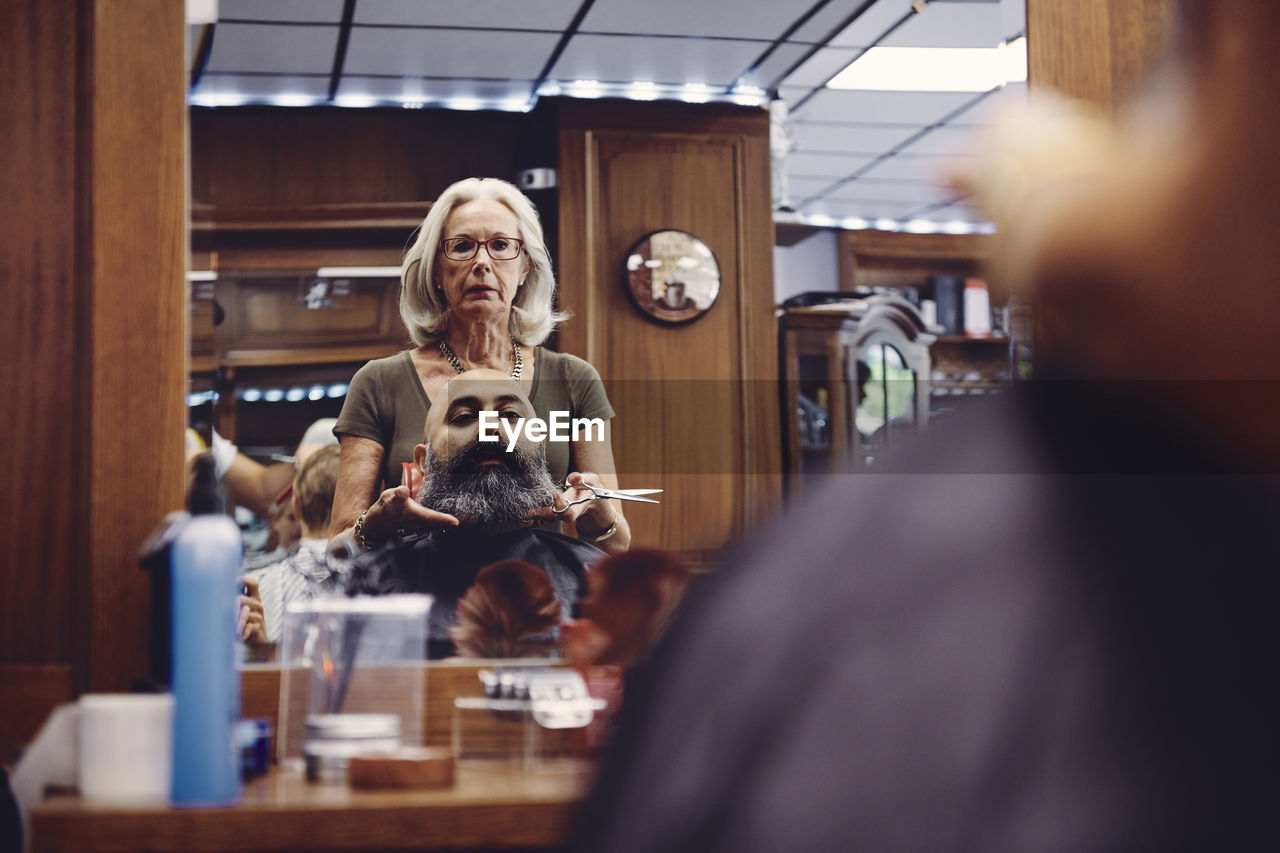 Woman cutting bald man beard in hair salon