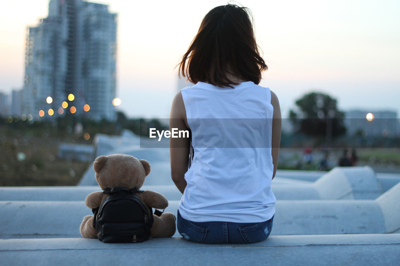 Rear view of woman with teddy bear sitting in city